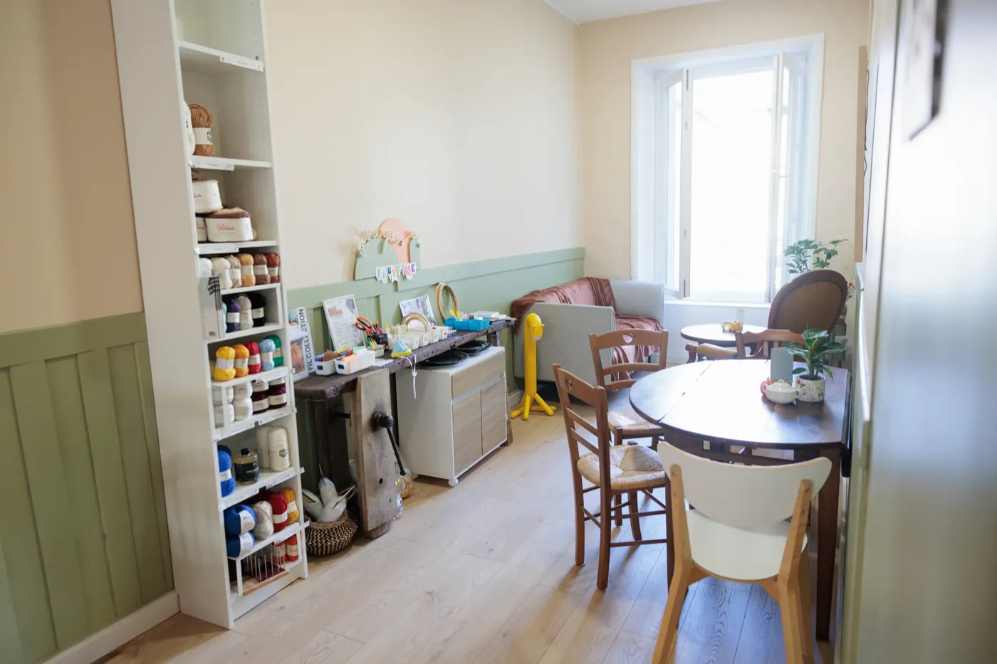 Intérieur du salon de thé : tables en bois, murs orange et étagères de matériel créatif